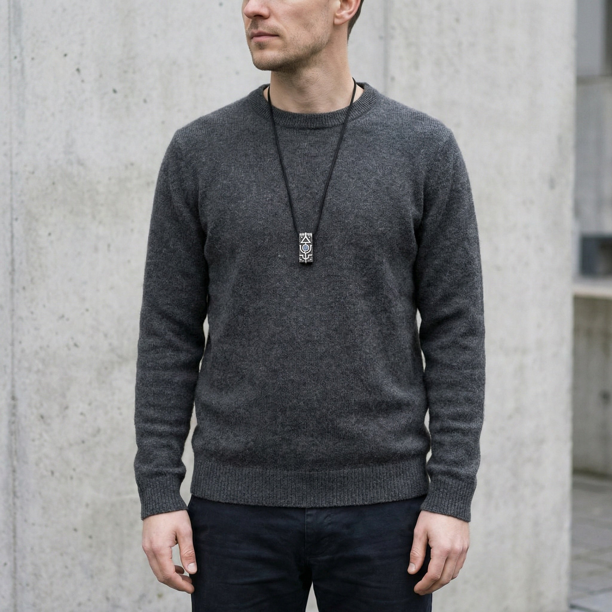 Man wearing a gray sweater against a concrete wall, mens handmade silver pendant 