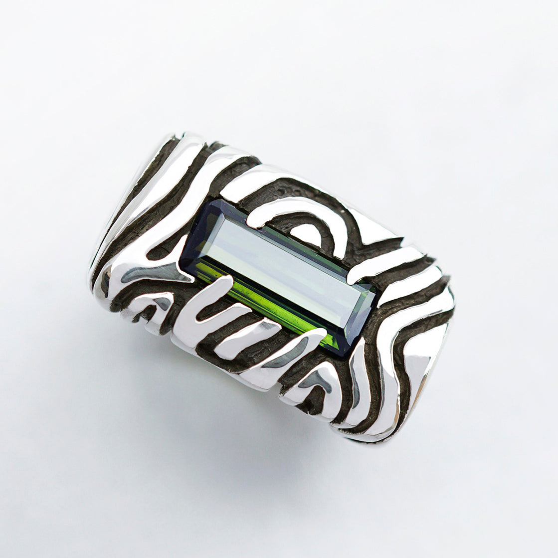 A sterling silver statement ring with a dark green stone set in a rectangular frame. The ring has a textured design with swirling lines. Geo collection by Moonique
