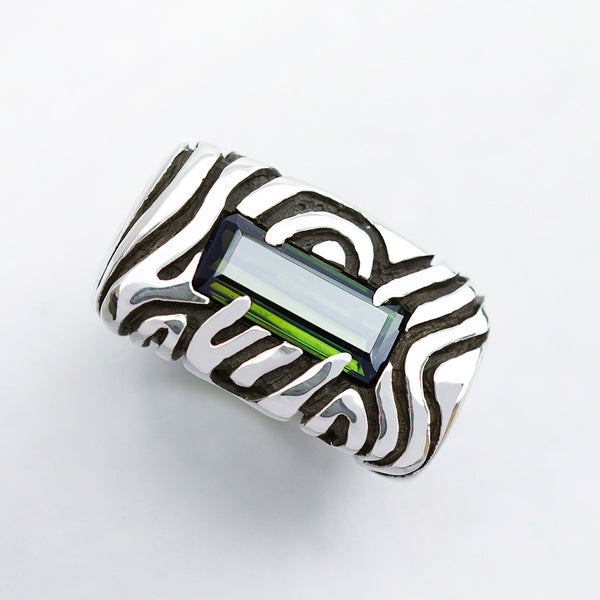A sterling silver statement ring with a dark green stone set in a rectangular frame. The ring has a textured design with swirling lines. Geo collection by Moonique