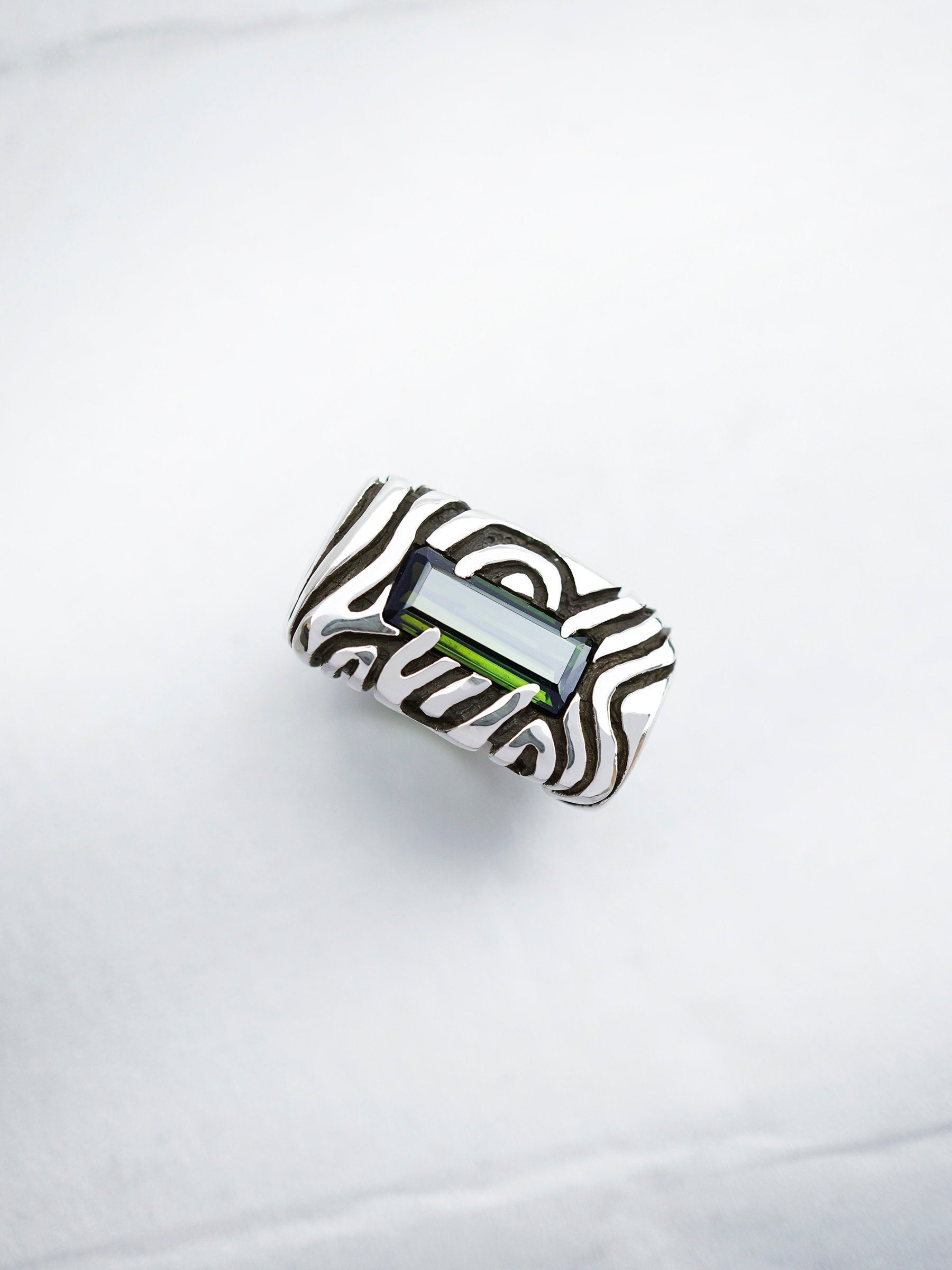 A sterling silver statement ring with a dark green stone set in a rectangular frame. The ring has a textured design with swirling lines. Geo collection by Moonique