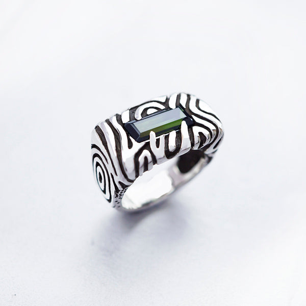 A sterling silver statement ring with a dark green stone set in a rectangular frame. The ring has a textured design with swirling lines. Geo collection by Moonique