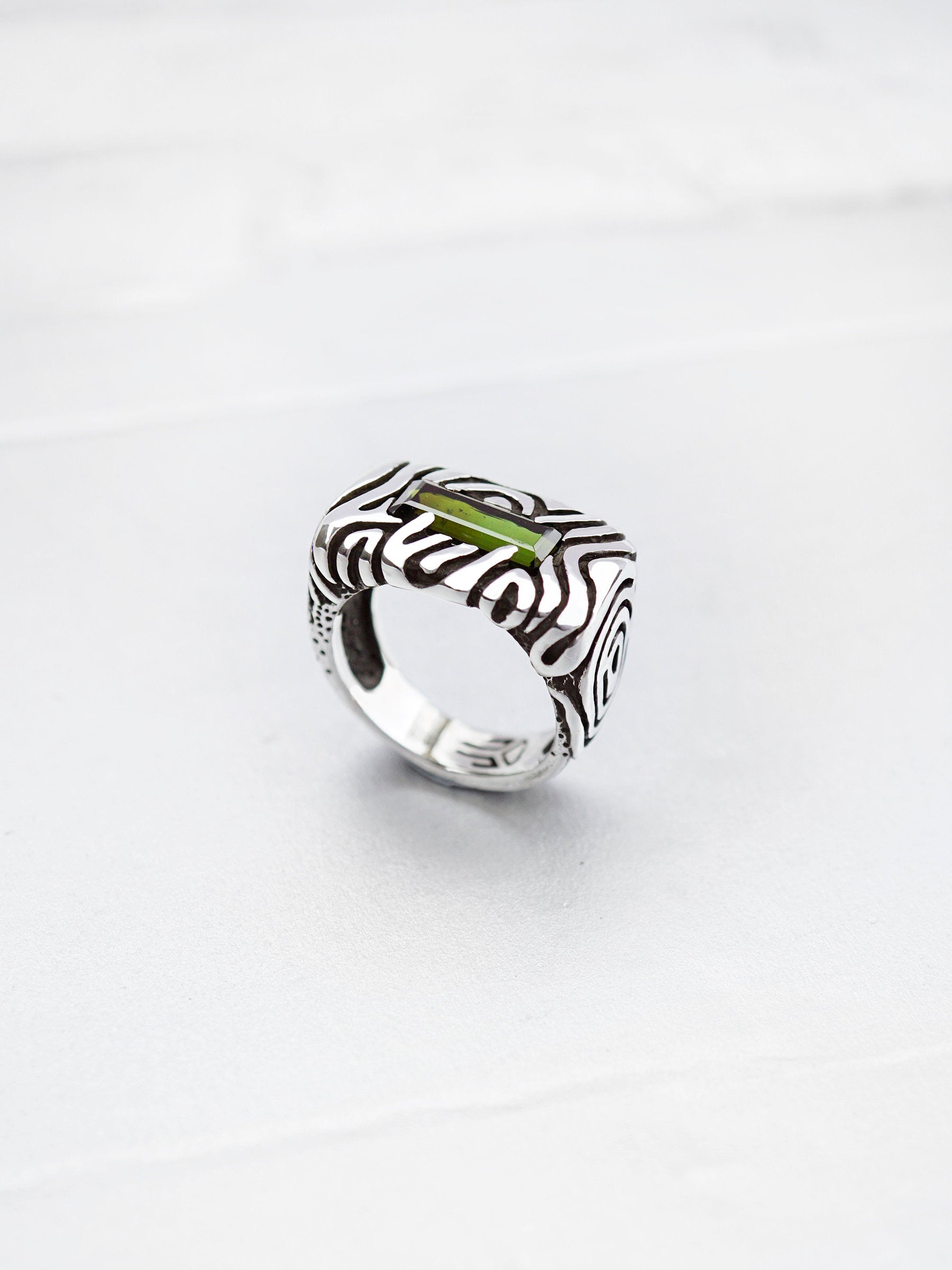 A sterling silver statement ring with a dark green stone set in a rectangular frame. The ring has a textured design with swirling lines. Geo collection by Moonique