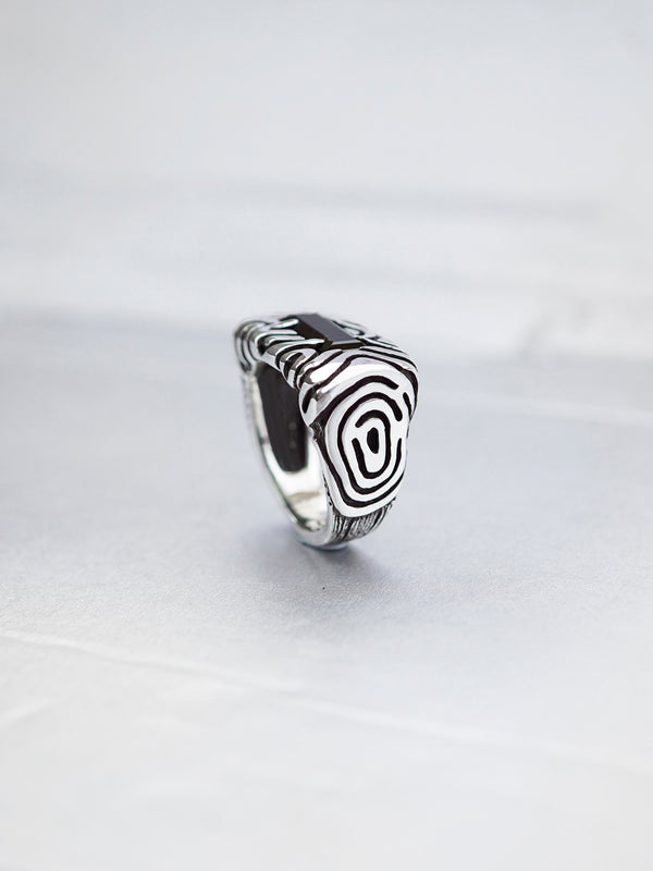 A sterling silver statement ring with a dark green stone set in a rectangular frame. The ring has a textured design with swirling lines. Geo collection by Moonique