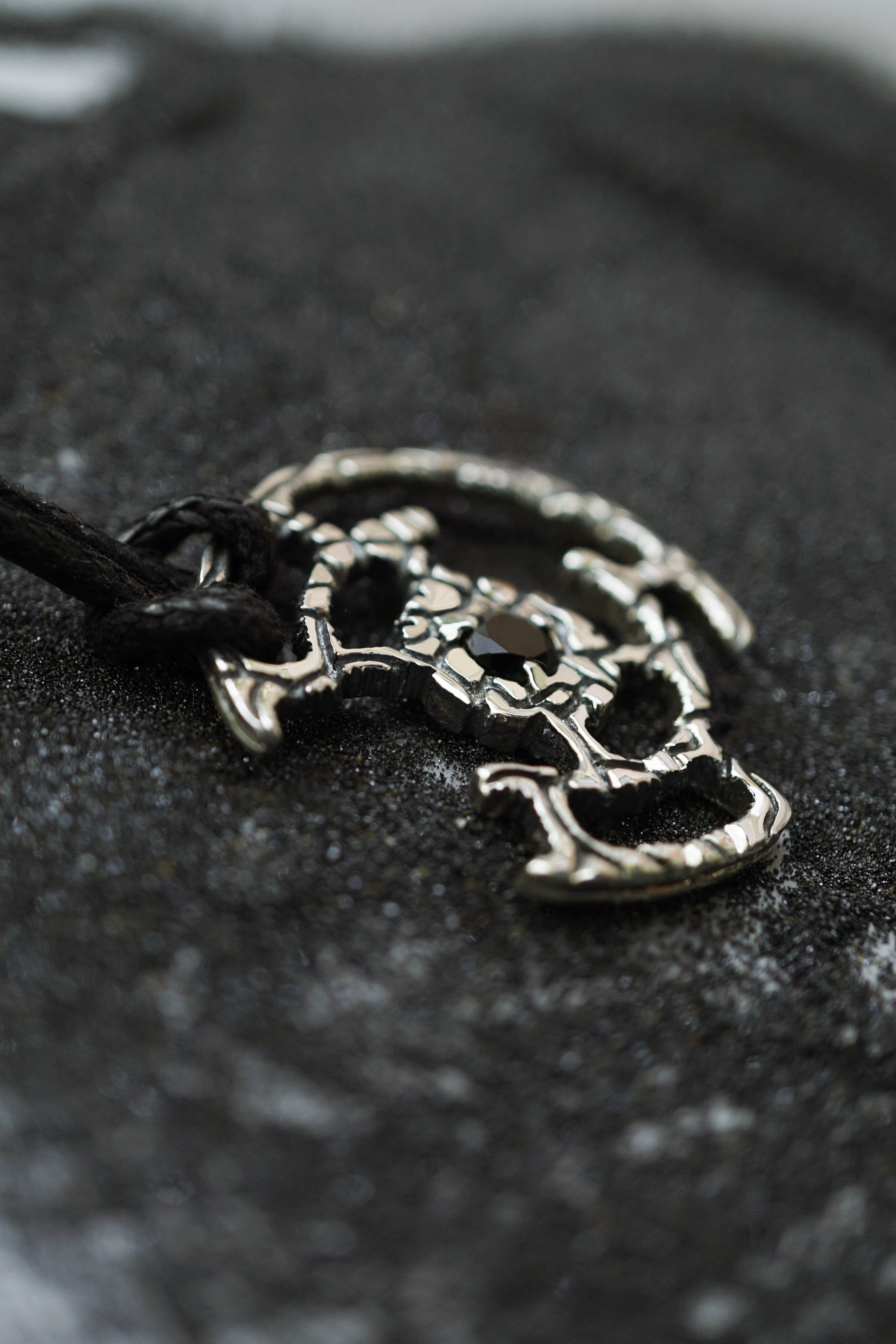 An oxidized solid sterling silver pendant with a green Tourmaline gemstone in the center. The pendant is in the shape of a circle with intricate designs. The pendant is hanging from a black cord. Cyberpunk design jewelry by Moonique.