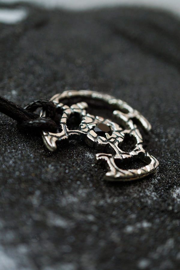 An oxidized solid sterling silver pendant with a green Tourmaline gemstone in the center. The pendant is in the shape of a circle with intricate designs. The pendant is hanging from a black cord. Cyberpunk design jewelry by Moonique.