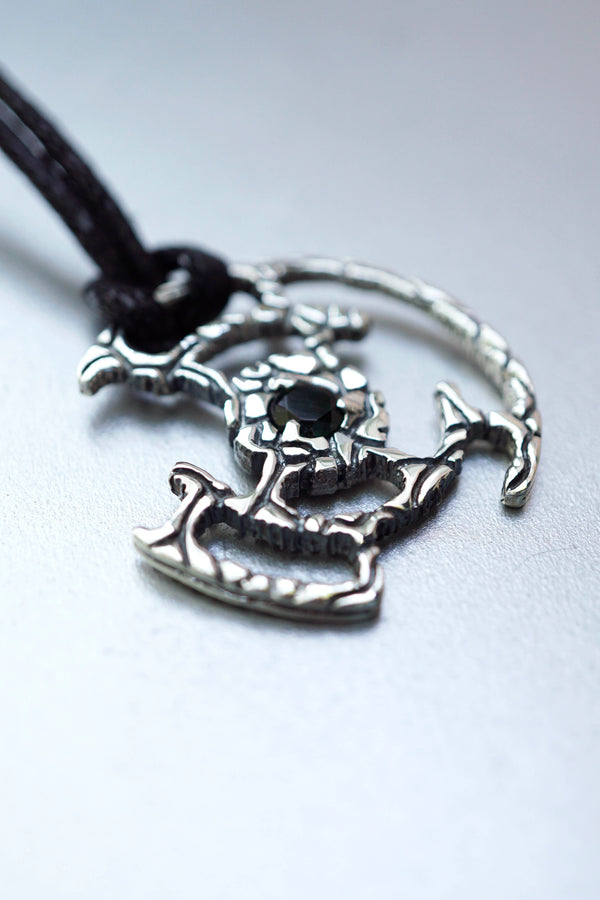 An oxidized solid sterling silver pendant with a green Tourmaline gemstone in the center. The pendant is in the shape of a circle with intricate designs. The pendant is hanging from a black cord. Cyberpunk design jewelry by Moonique.