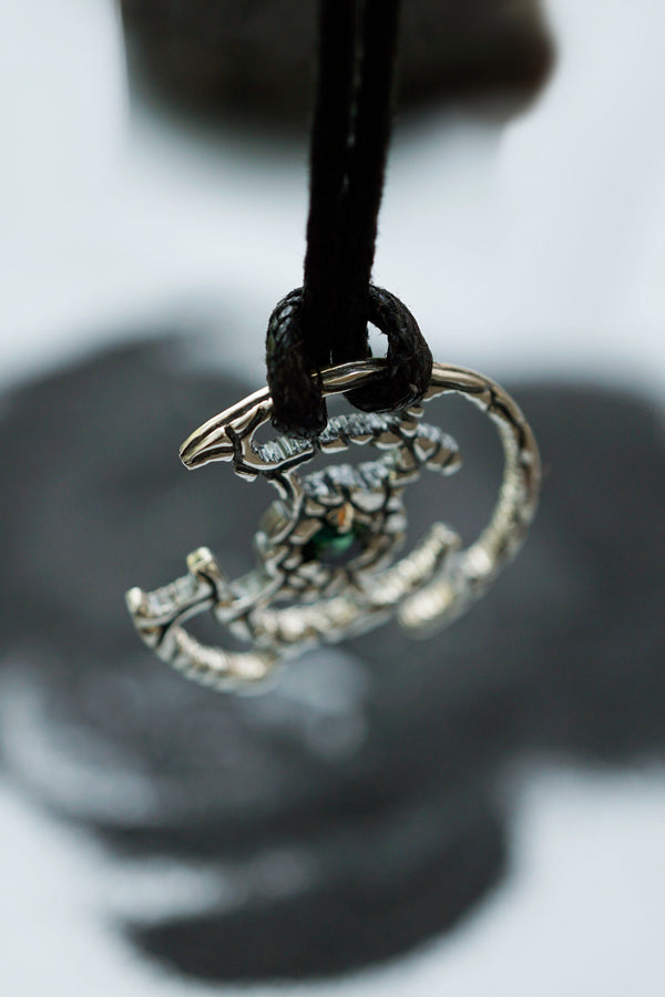 An oxidized solid sterling silver pendant with a green Tourmaline gemstone in the center. The pendant is in the shape of a circle with intricate designs. The pendant is hanging from a black cord. Cyberpunk design jewelry by Moonique.