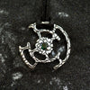 An oxidized solid sterling silver pendant with a green Tourmaline gemstone in the center. The pendant is in the shape of a circle with intricate designs. The pendant is hanging from a black cord. Cyberpunk design jewelry by Moonique.