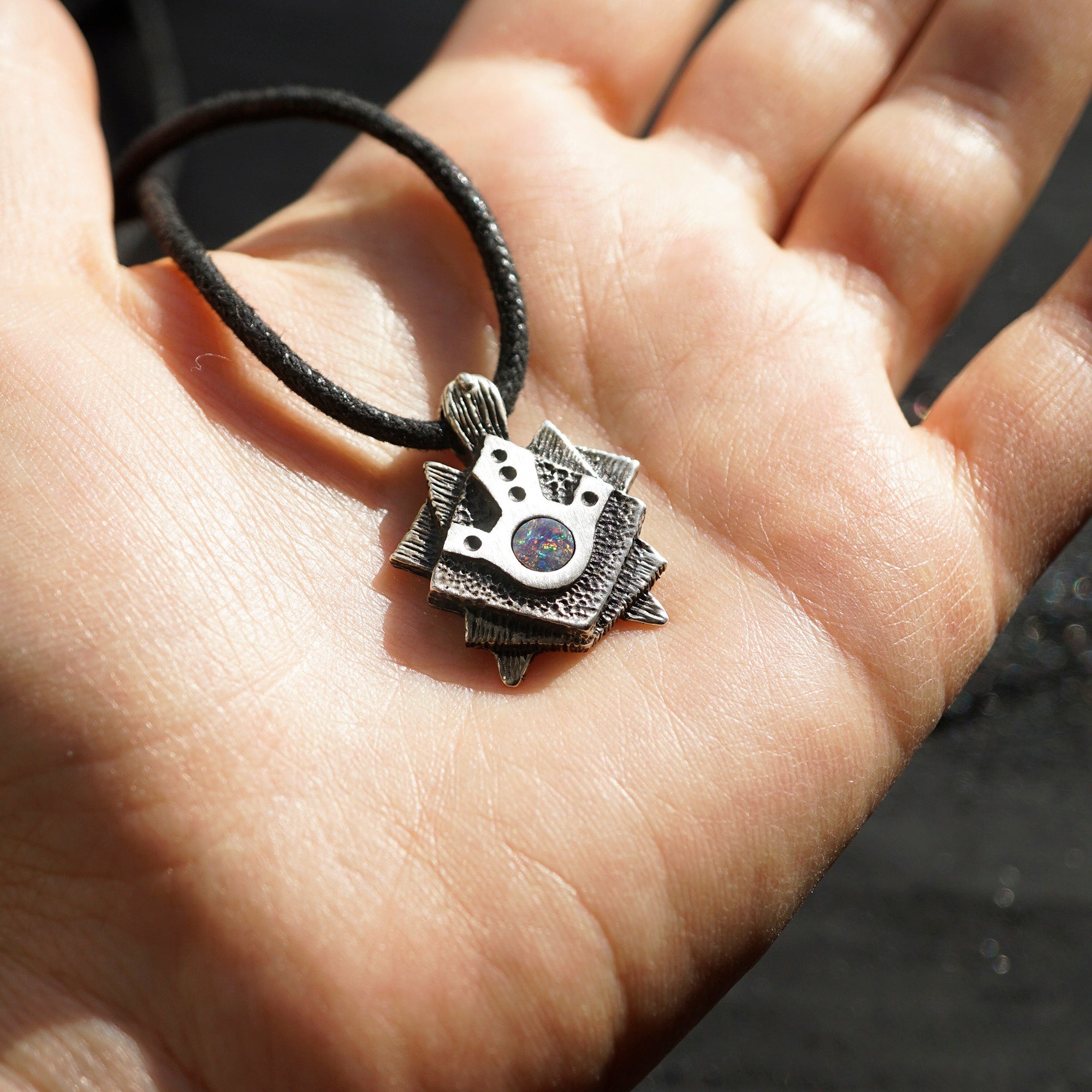 A handmade solid oxidized sterling silver pendant with a geometric Tortoise design and a natural round blue opal gemstone in the center. The pendant is on a wooden surface. Turtle unique pendant by moonique