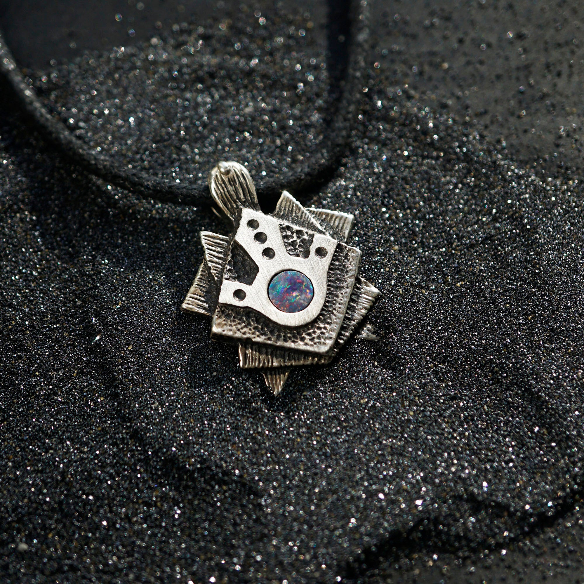 A handmade solid oxidized sterling silver pendant with a geometric Tortoise design and a natural round blue opal gemstone in the center. The pendant is on a wooden surface. Turtle unique pendant by moonique