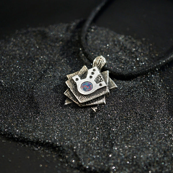 A handmade solid oxidized sterling silver pendant with a geometric Tortoise design and a natural round blue opal gemstone in the center. The pendant is on a wooden surface. Turtle unique pendant by moonique