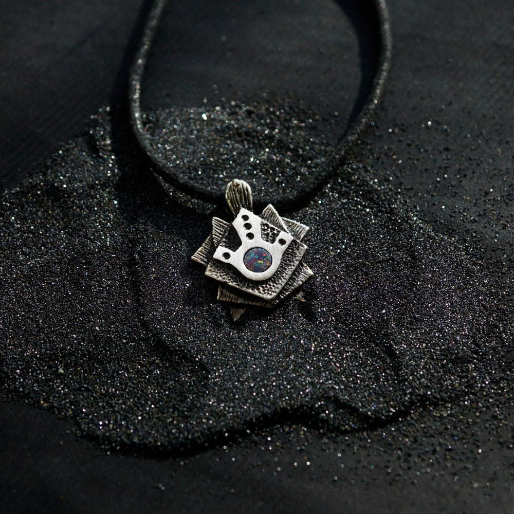 A handmade solid oxidized sterling silver pendant with a geometric Tortoise design and a natural round blue opal gemstone in the center. The pendant is on a wooden surface. Turtle unique pendant by moonique