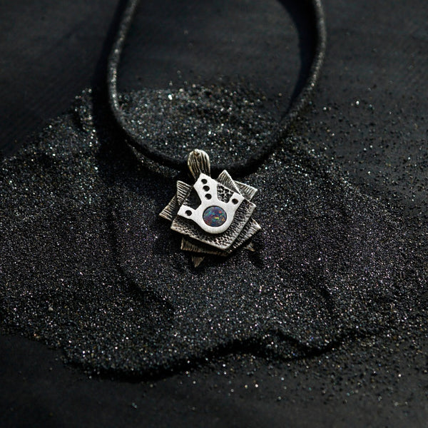 A handmade solid oxidized sterling silver pendant with a geometric Tortoise design and a natural round blue opal gemstone in the center. The pendant is on a wooden surface. Turtle unique pendant by moonique