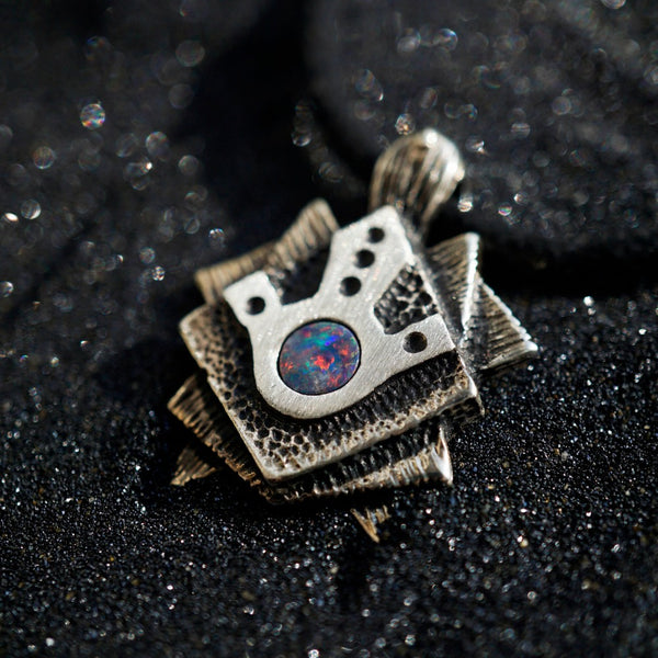 A handmade solid oxidized sterling silver pendant with a geometric Tortoise design and a natural round blue opal gemstone in the center. The pendant is on a wooden surface. Turtle unique pendant by moonique
