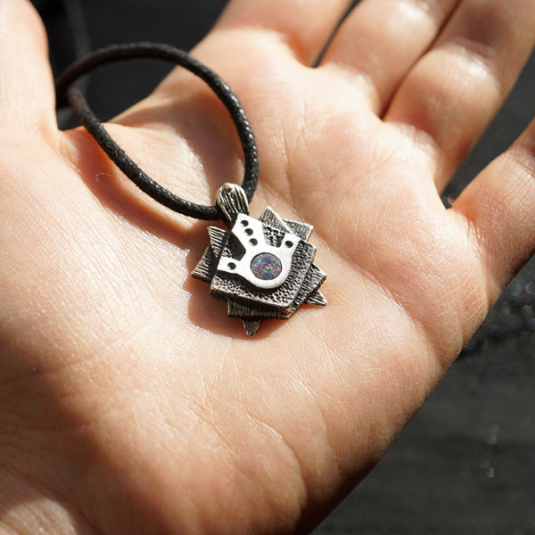A handmade solid oxidized sterling silver pendant with a geometric Tortoise design and a natural round blue opal gemstone in the center. The pendant is on a wooden surface. Turtle unique pendant by moonique